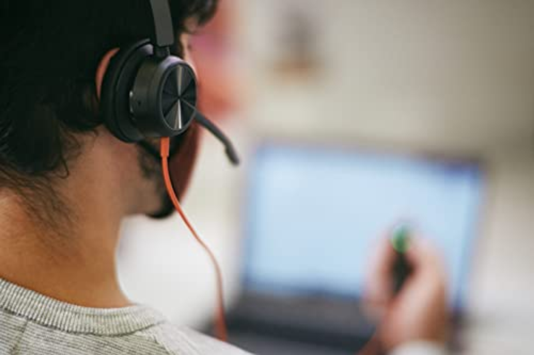 Persona usando auriculares negros, mirando la pantalla de una laptop.