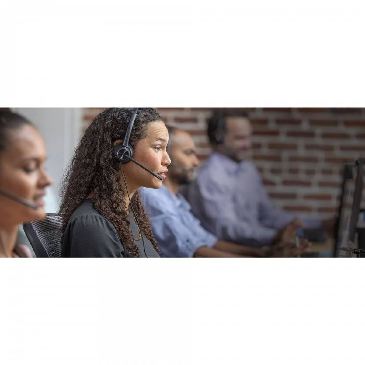 Frau mit Headset in Callcenter-Umgebung. Andere Personen sind im Hintergrund unscharf.