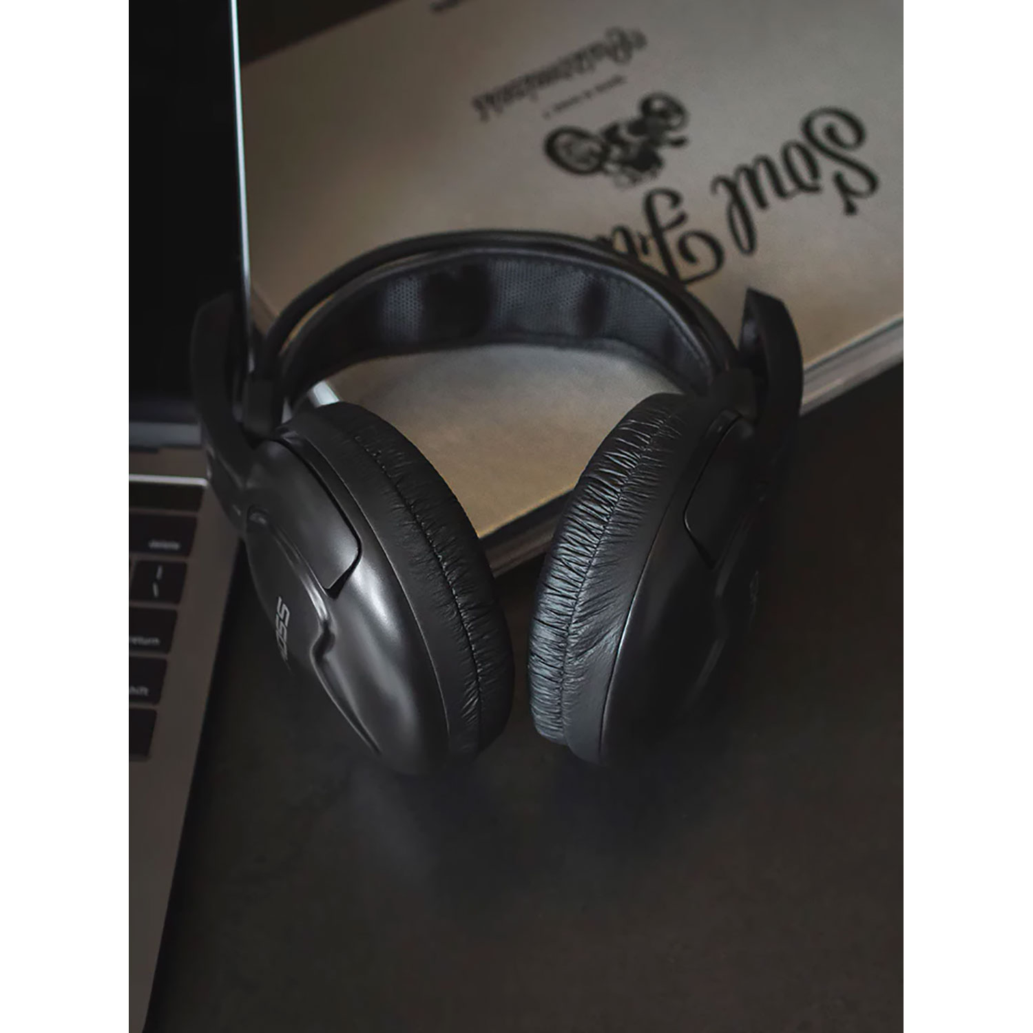Casque noir sur surface noire, à côté d'un ordinateur portable et d'un livre.