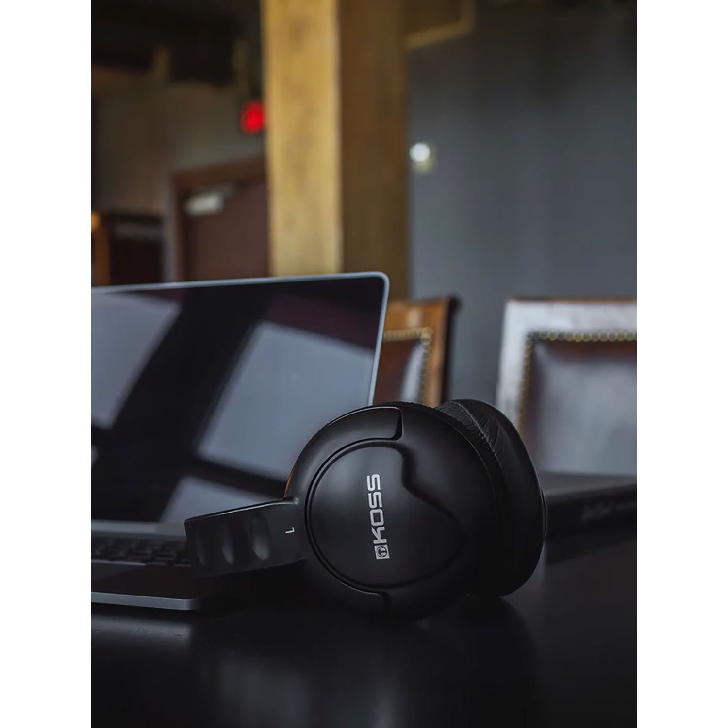 Casque Koss noir posé sur un ordinateur portable sur une table en bois sombre.