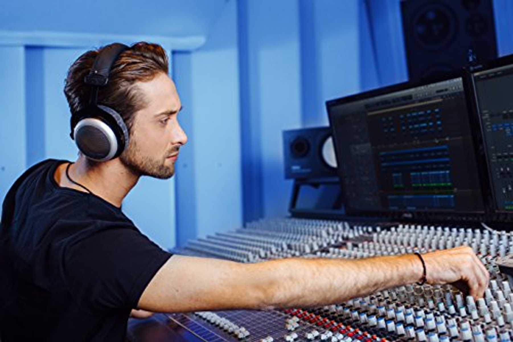 Mężczyzna używa konsoli mikserskiej, w słuchawkach, w studio nagraniowym.