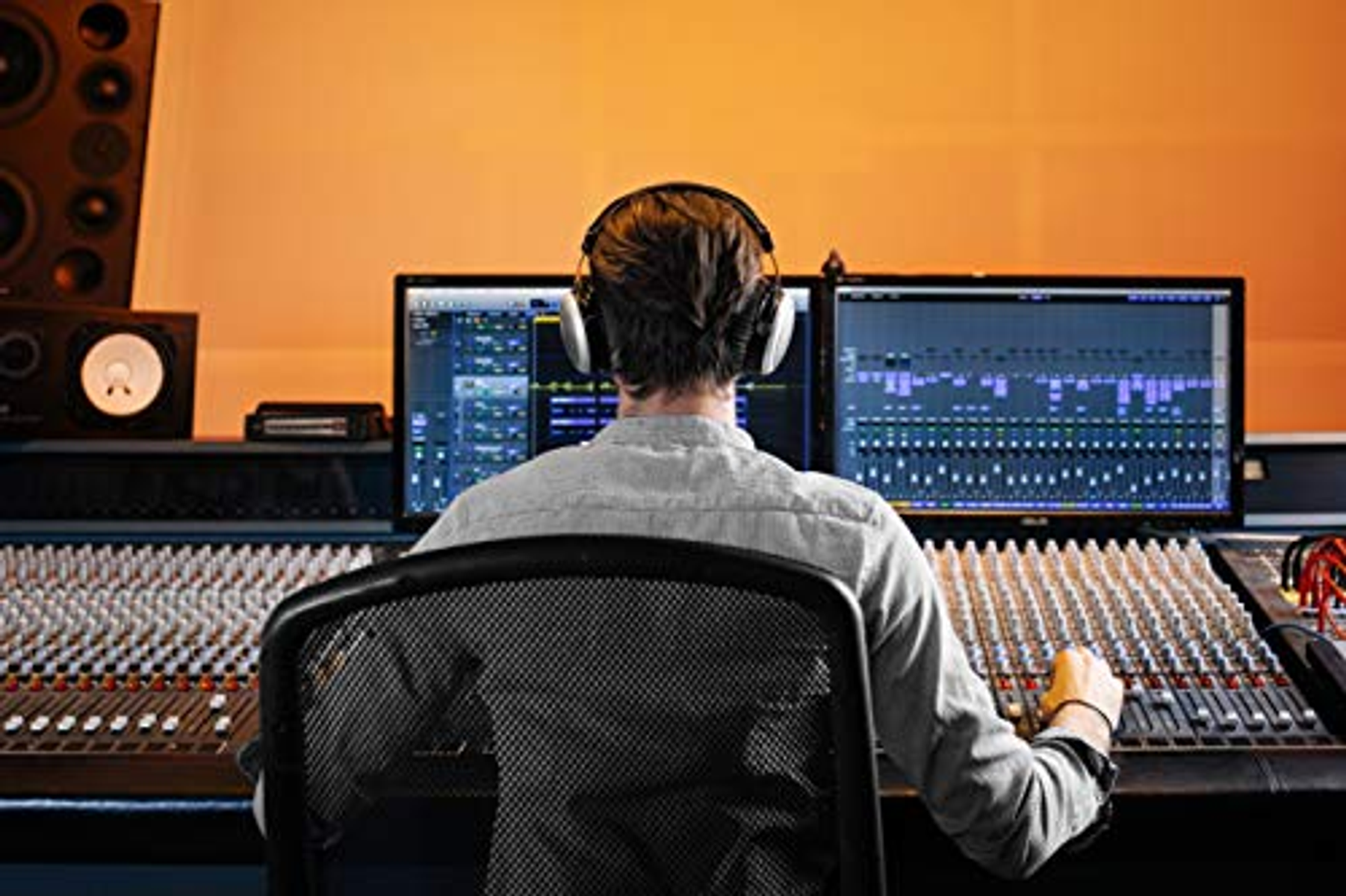 Osoba w słuchawkach w studio. Obecne dwa monitory komputerowe i mikser.
