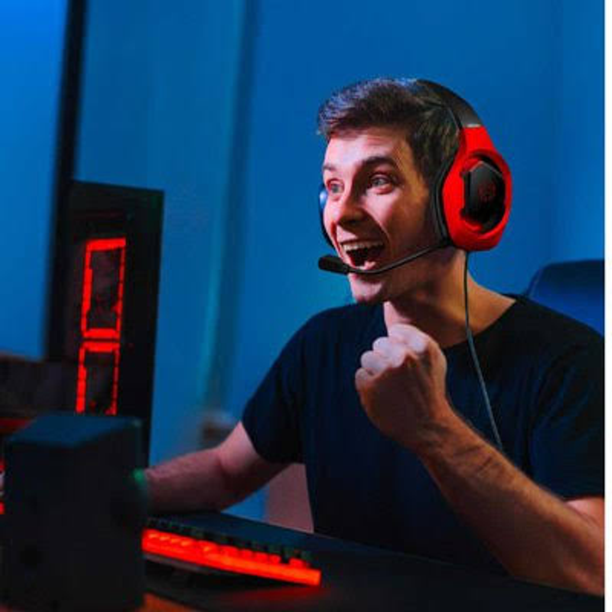 Mężczyzna w czerwonym zestawie słuchawkowym do gier, uśmiechnięty, gra w grę wideo, z czerwonym oświetleniem.