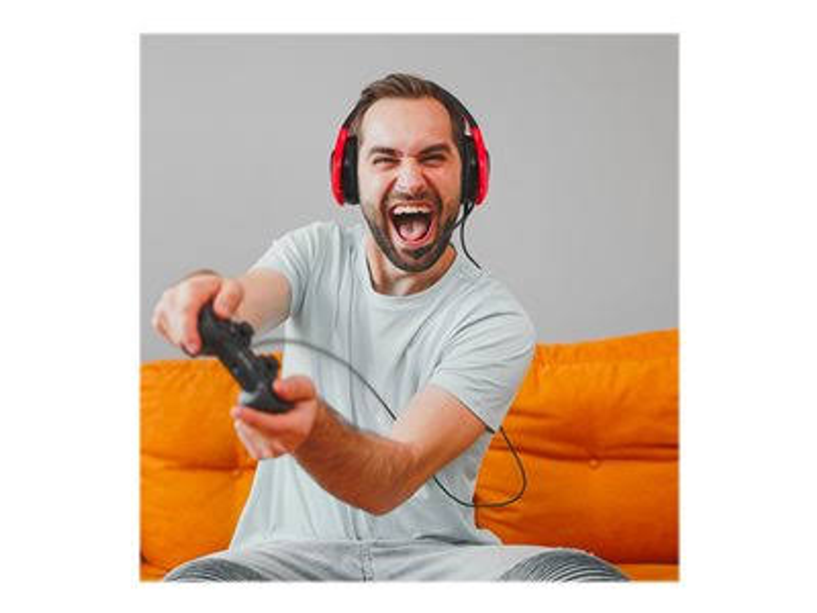 Mężczyzna gra w grę wideo w słuchawkach. Krzyczy i trzyma kontroler. Sofa w tle.