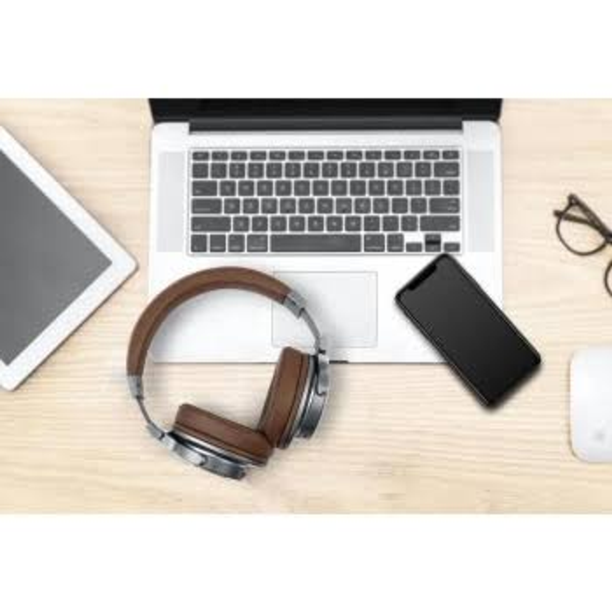 Laptop, tablet, telefon, słuchawki i mysz na drewnianym stole. Wszystkie to przedmioty techniczne.