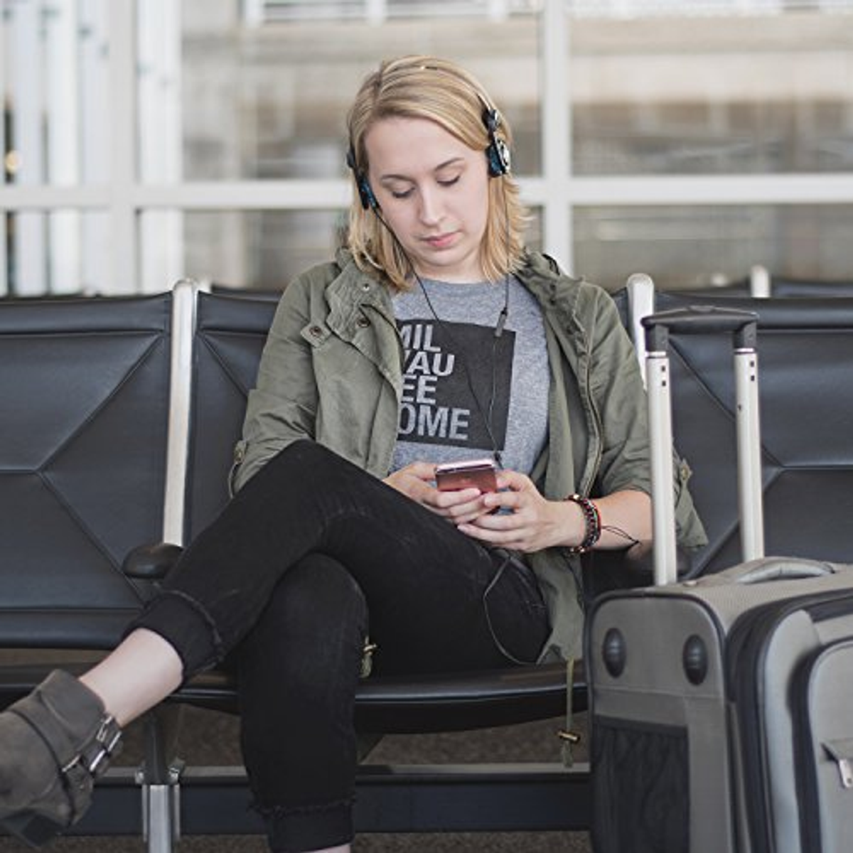 Kobieta w słuchawkach, siedząca na lotnisku i korzystająca z telefonu.