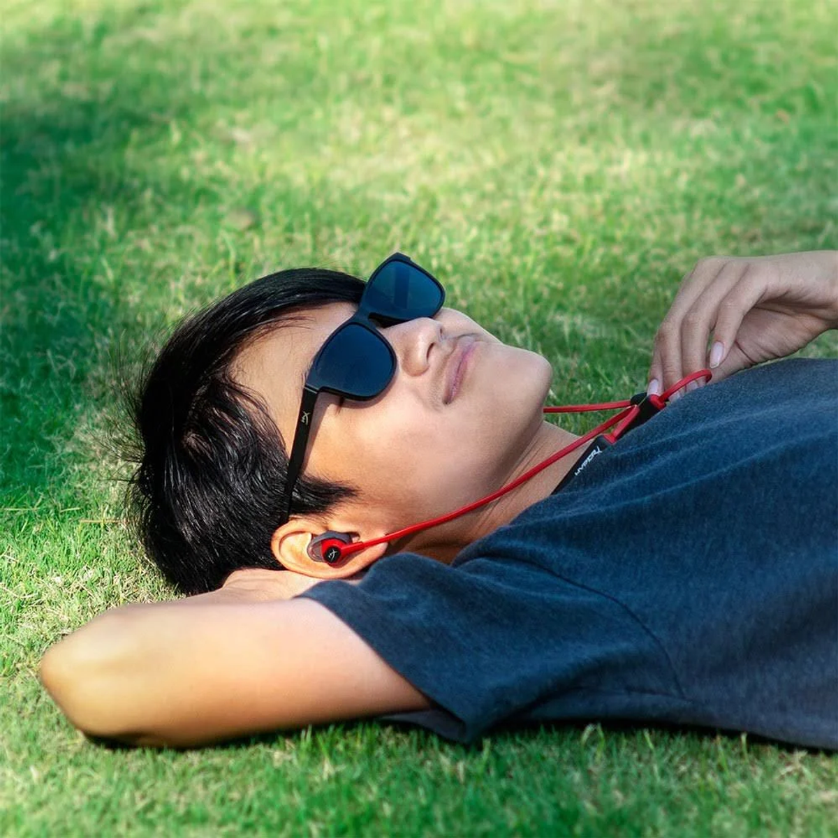 Mężczyzna w okularach przeciwsłonecznych i czerwonych słuchawkach dousznych leżący na trawie.