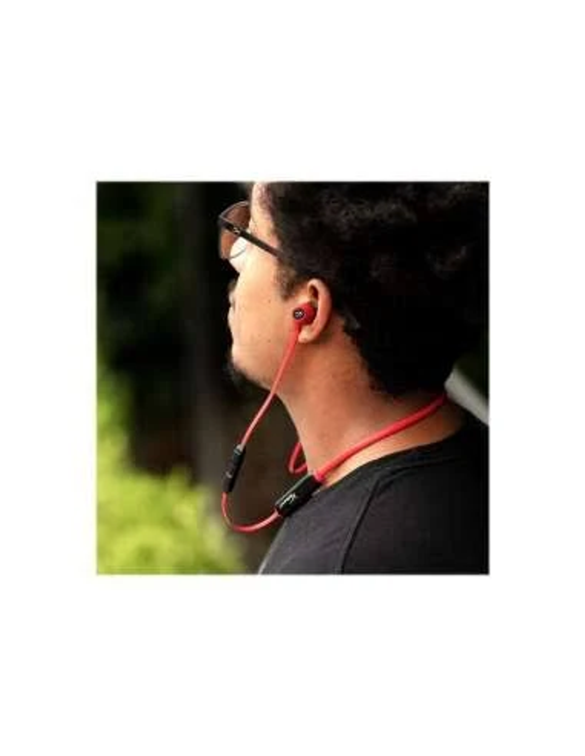 Mężczyzna w okularach przeciwsłonecznych i czarnej koszuli ze słuchawkami z czerwoną opaską na szyję.