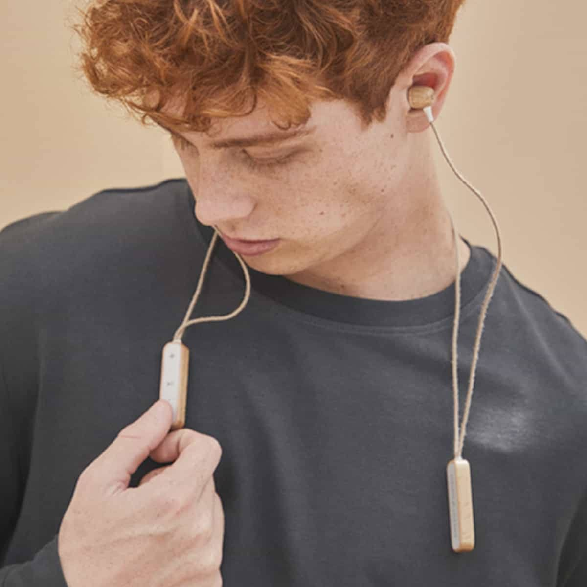 Ein Mann mit roten Haaren trägt Ohrhörer aus Holz. Er hält ein Steuerungselement aus Holz.