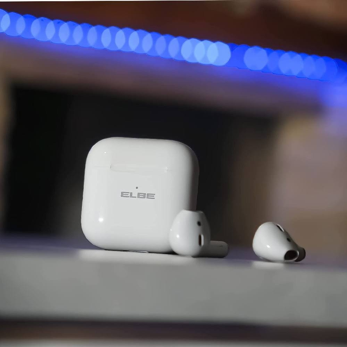 Białe słuchawki i etui ładujące na stole, z niebieskim światłem. Rozmyte tło.