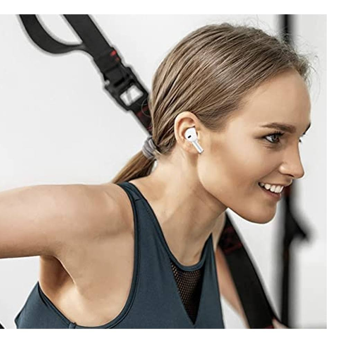 Kobieta w białych słuchawkach i pasach do ćwiczeń, uśmiechnięta, na białym tle.