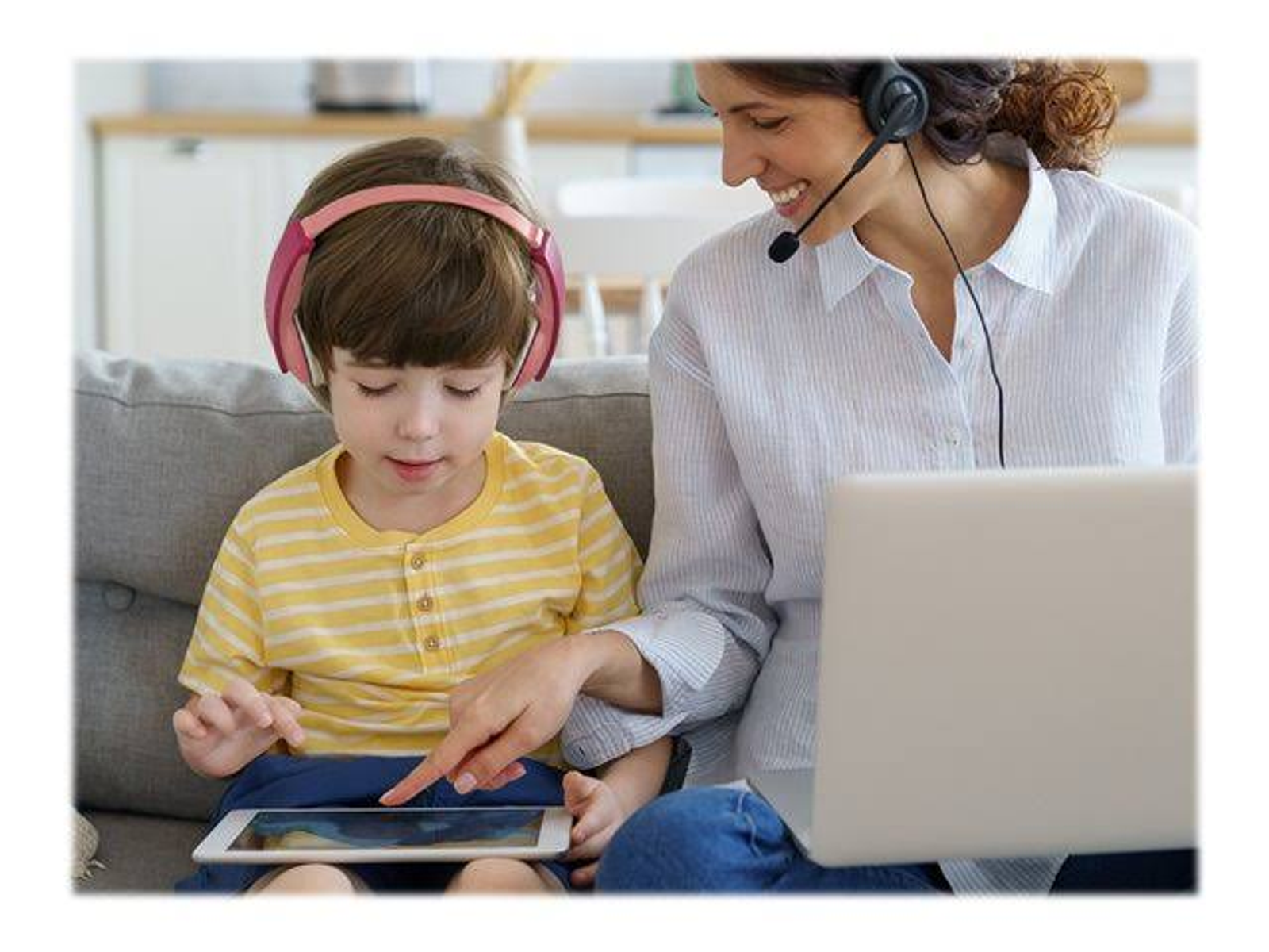 Una donna e un bambino usano un tablet con le cuffie su un divano. Un laptop è aperto.