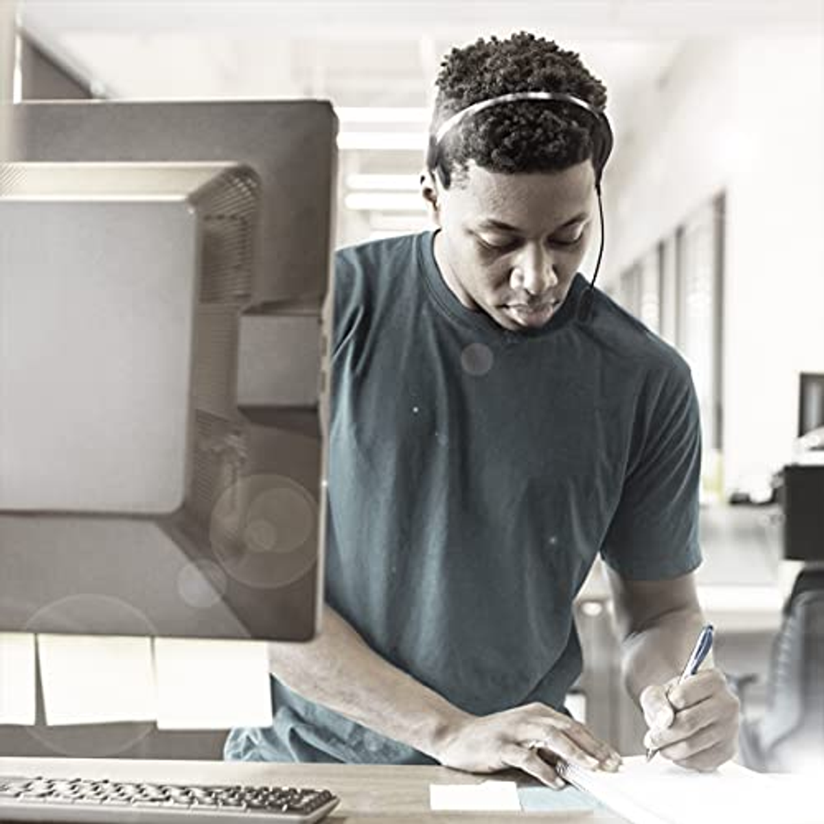 Mężczyzna piszący na papierze, monitor komputera na pierwszym planie.