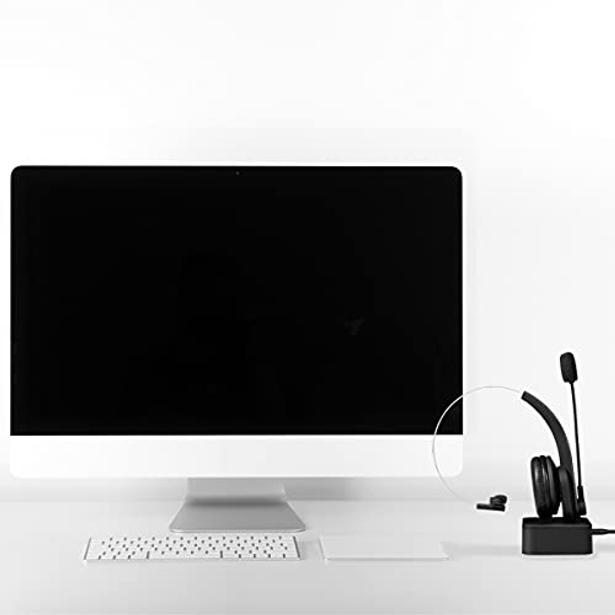 Monitor komputera, klawiatura i zestaw słuchawkowy na białym biurku. Ekran jest czarny.