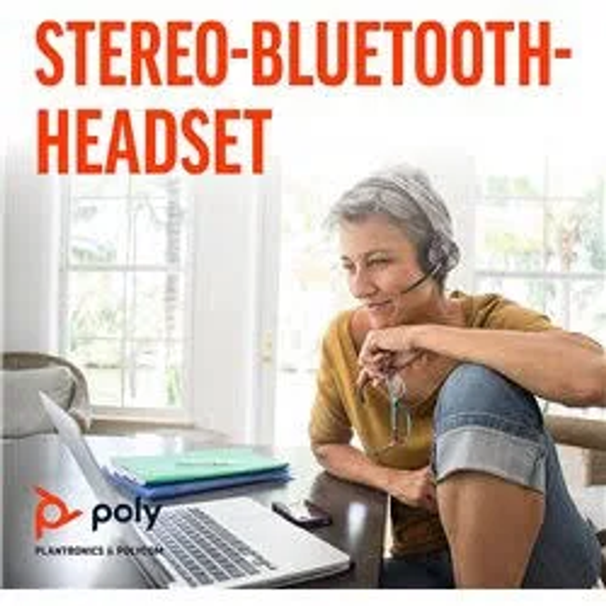 Kobieta w zestawie słuchawkowym siedzi przy biurku. Na biurku znajduje się również laptop i telefon.