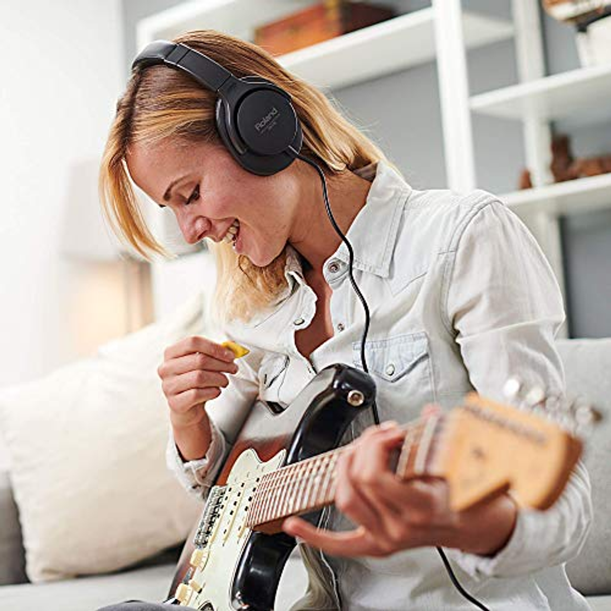Femme jouant de la guitare avec un casque. La guitare est une Fender. Elle sourit.