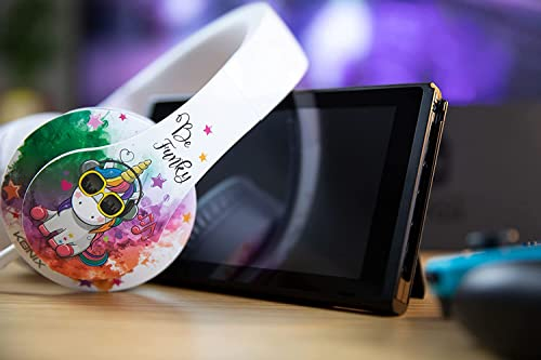 Białe słuchawki z jednorożcem, czarny Nintendo Switch i niebieski kontroler.