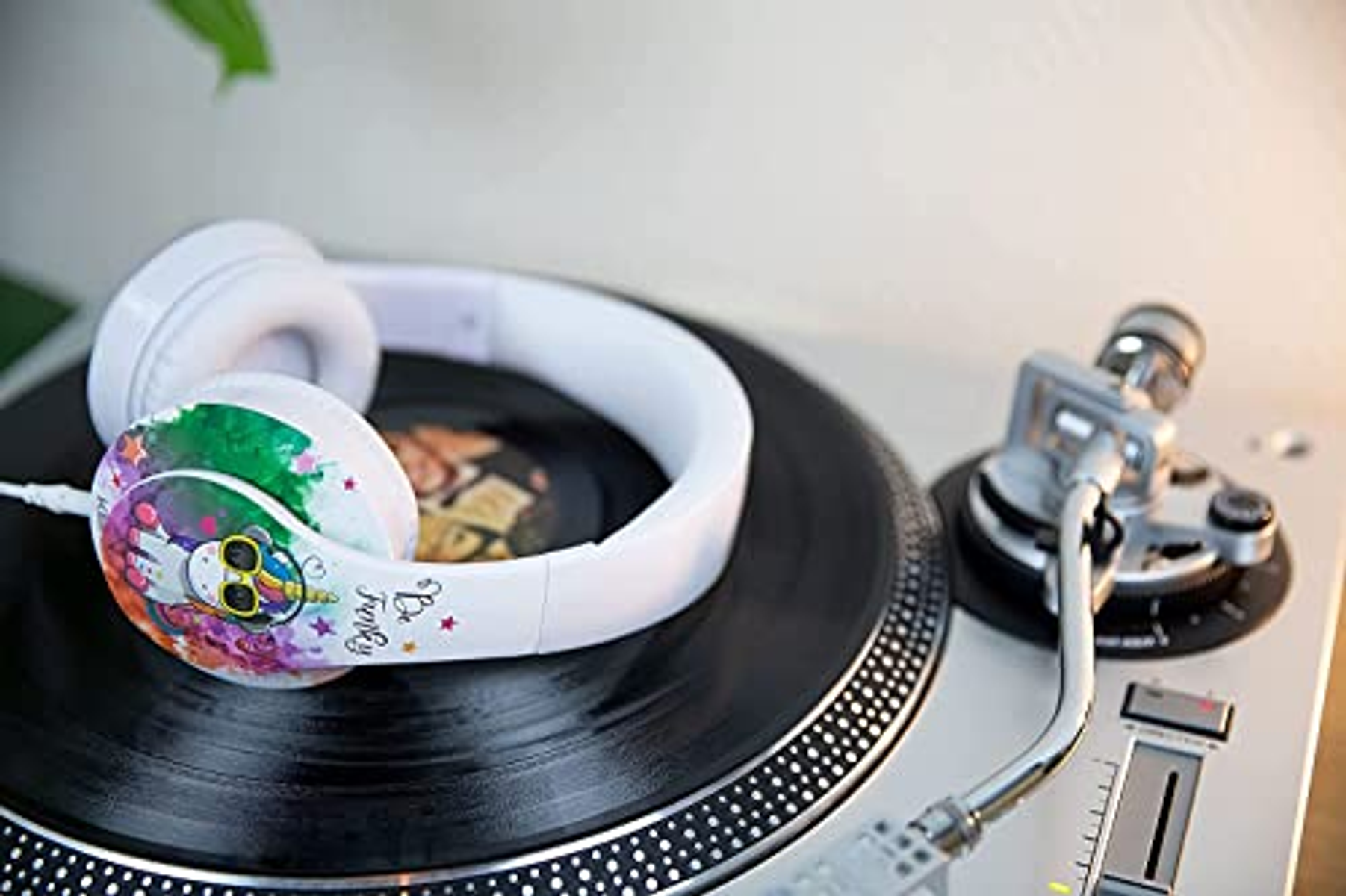 Białe słuchawki z kolorowym wzorem jednorożca na nauszniku, na gramofonie.