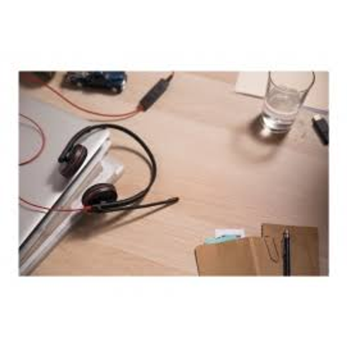 Casque sur une table en bois. Il y a un verre et des papiers sur la table. Le casque est noir.