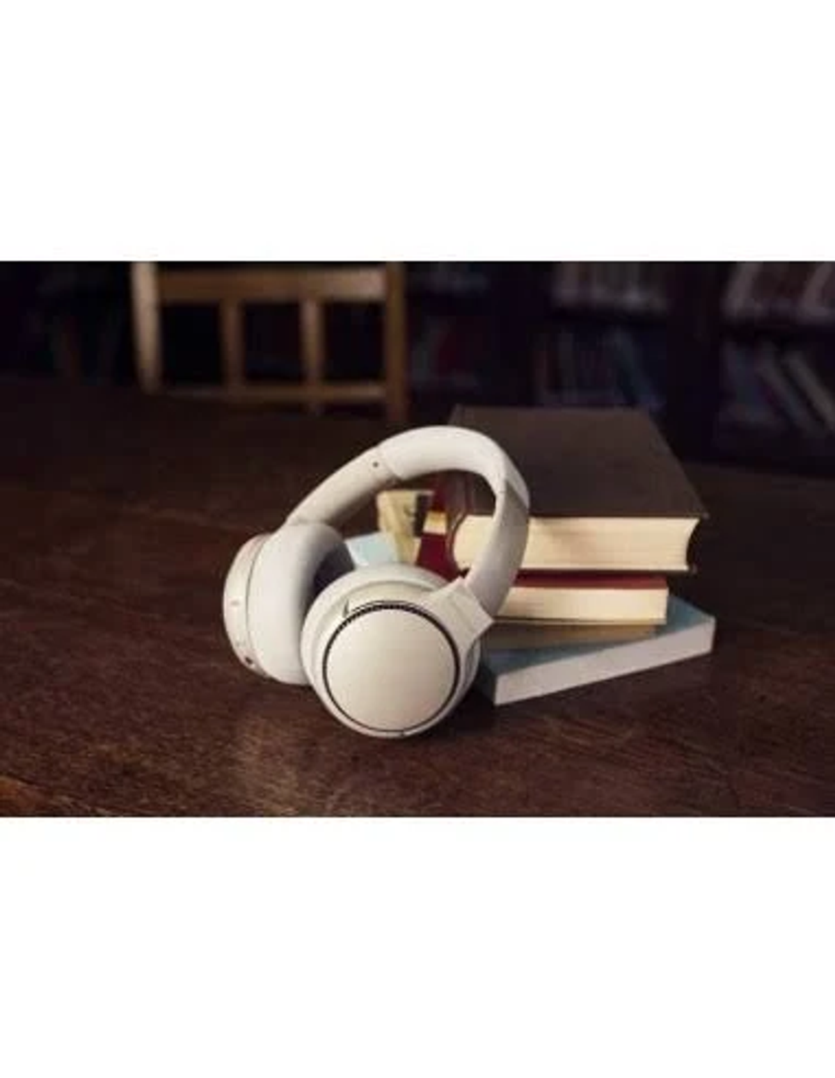 Weiße Kopfhörer auf einem Holztisch neben Büchern.