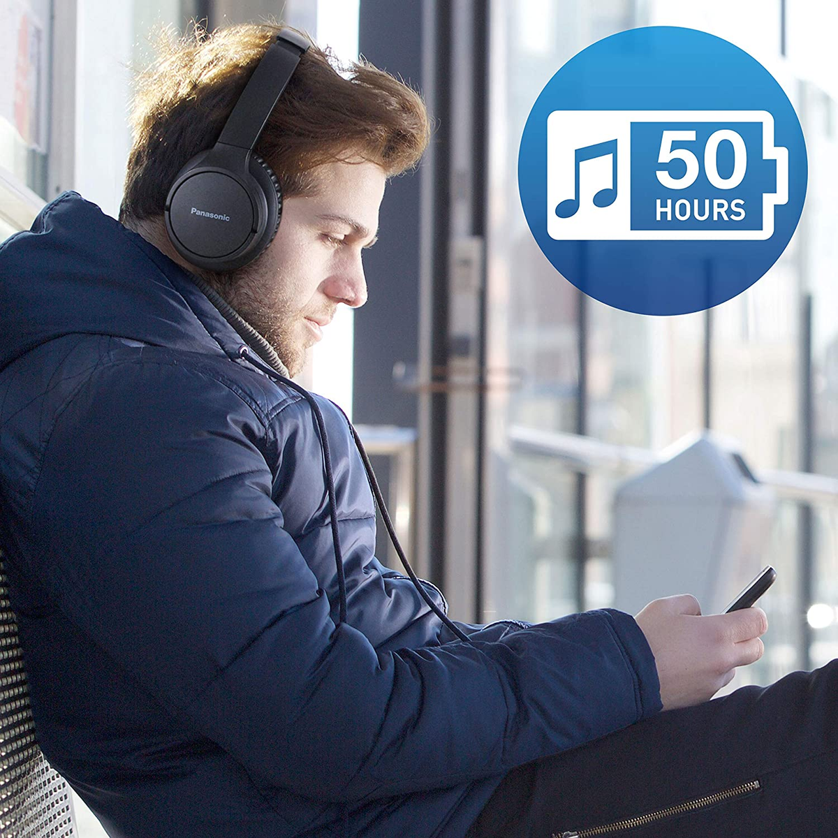 Mężczyzna w słuchawkach, patrzący na telefon, z ikoną baterii.