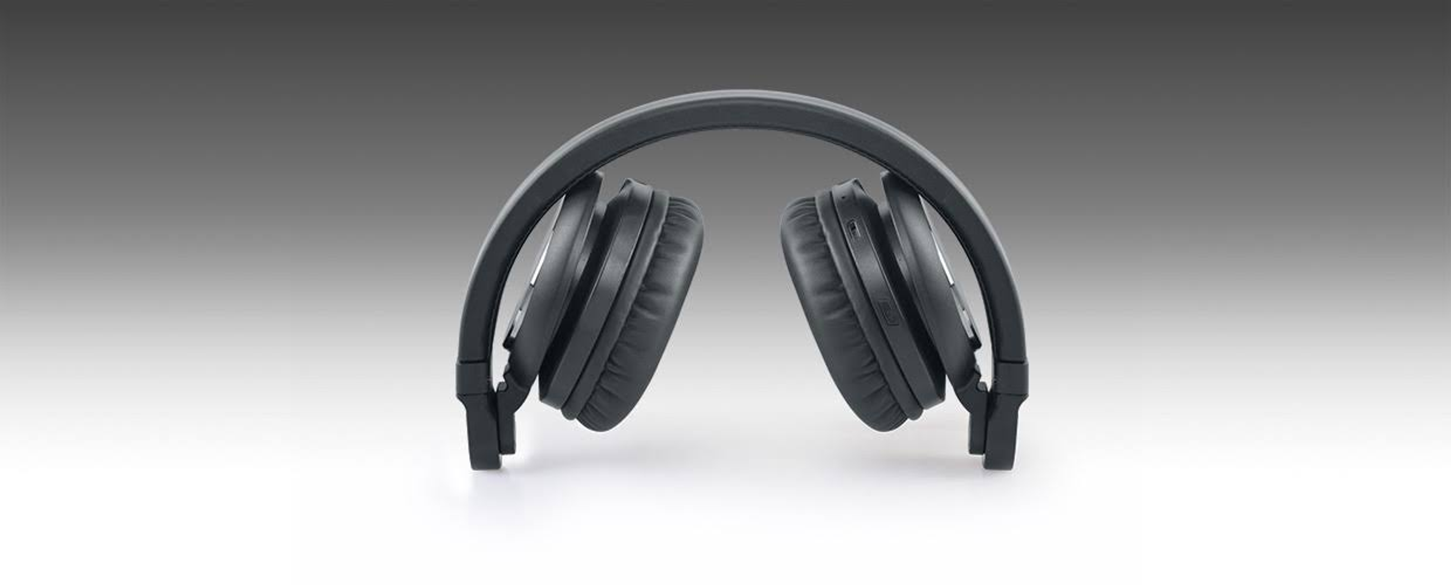 Czarne słuchawki złożone. Słuchawki leżą na białej powierzchni. Tło jest szare.