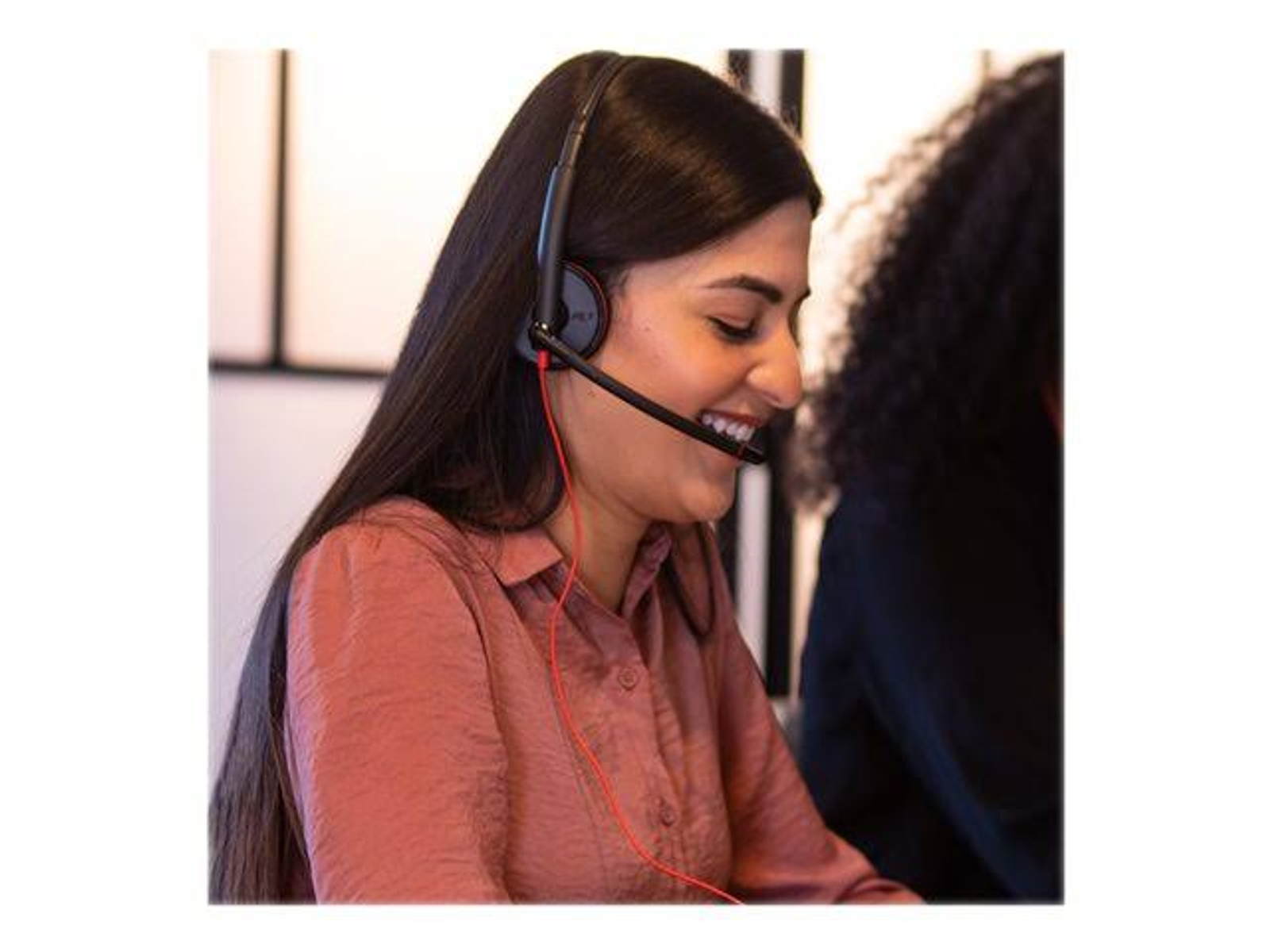 Kobieta w zestawie słuchawkowym, uśmiechnięta, z długimi, ciemnymi włosami.