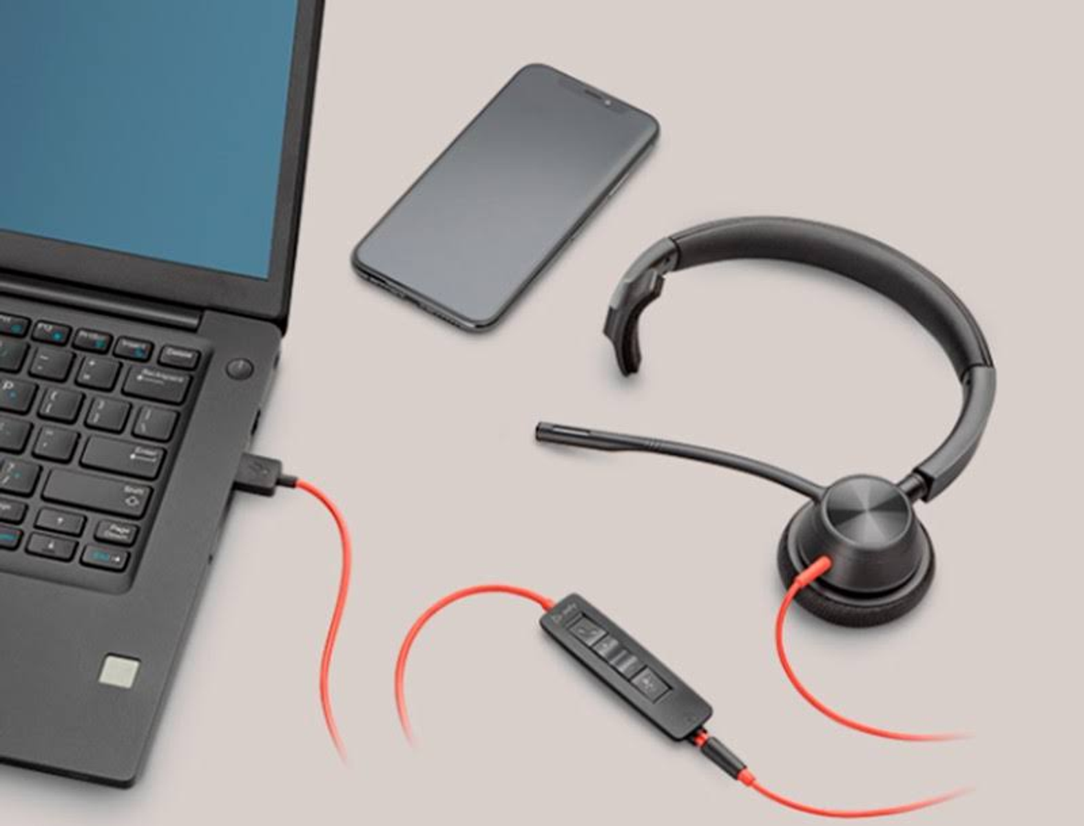 Laptop ze słuchawkami i telefonem na białej powierzchni. Słuchawki są podłączone.