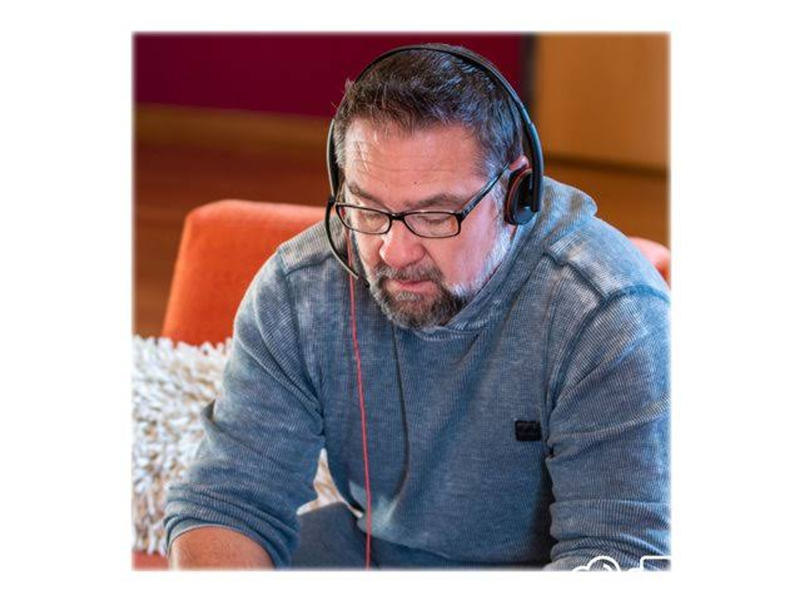 Mężczyzna w okularach noszący zestaw słuchawkowy, w otoczeniu biurowym. Czerwony kabel.