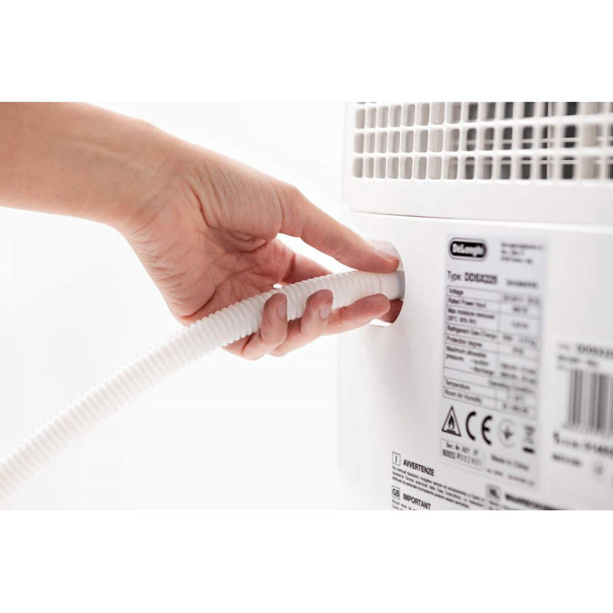 Dłoń trzyma białą, elastyczną rurę. Rura jest podłączona do białego urządzenia.