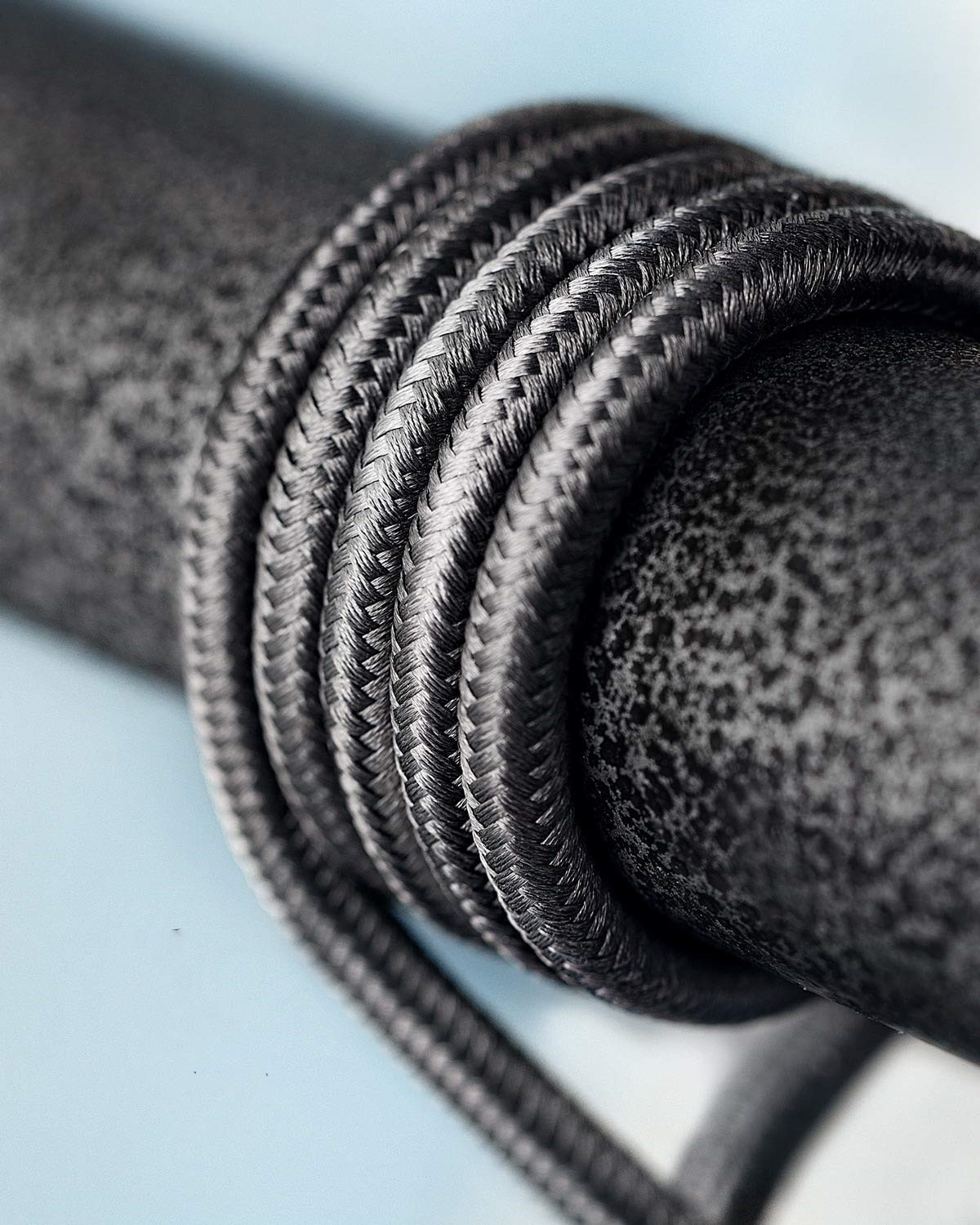 Czarny pleciony kabel owinięty wokół ciemnego metalowego pręta. Zbliżenie.