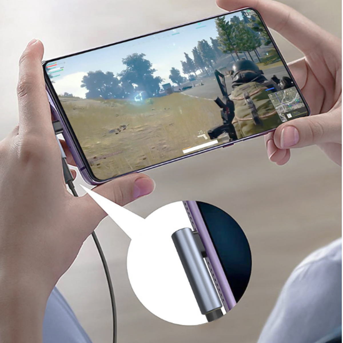 Ręce trzymające telefon, gra. Telefon jest podłączony do srebrnego adaptera.