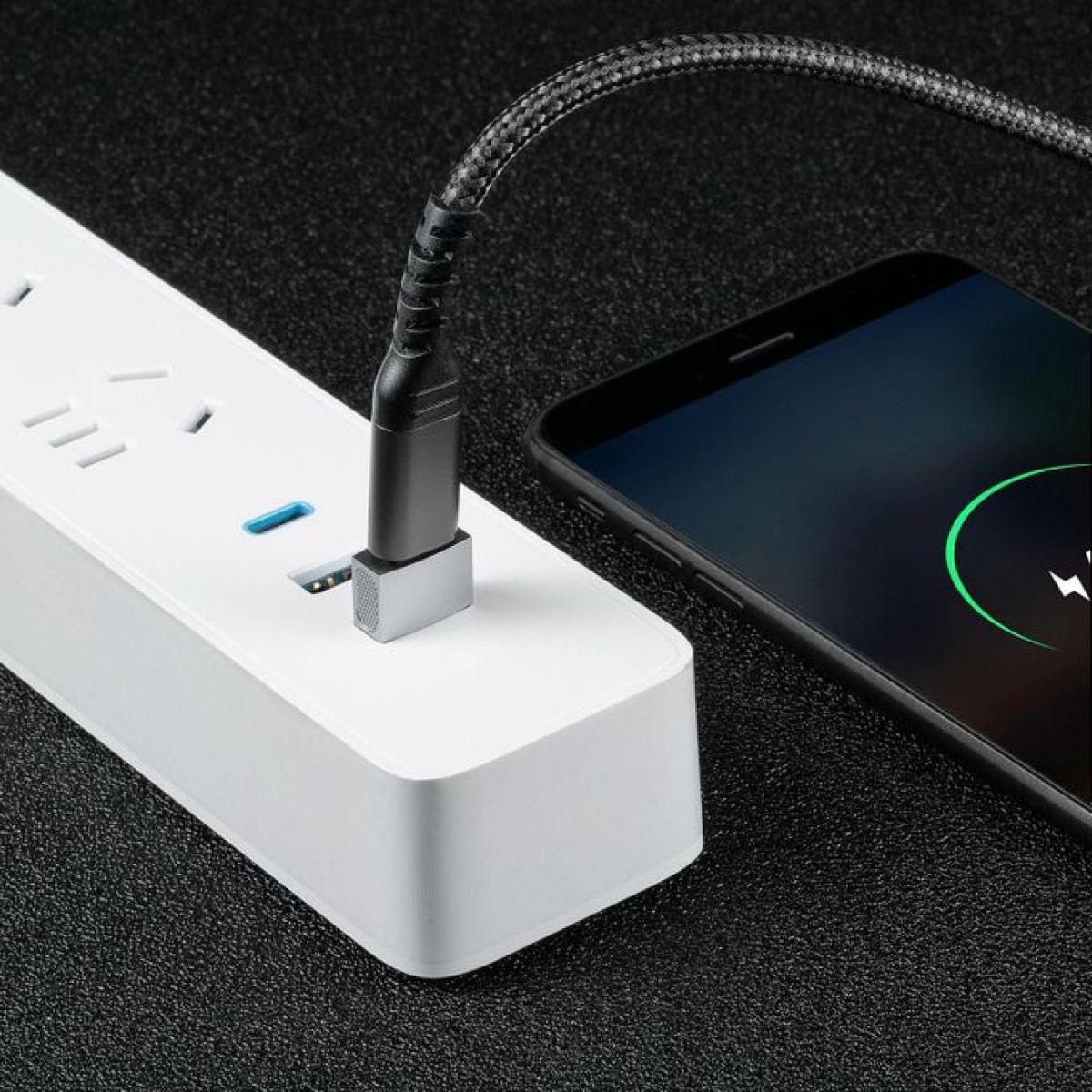 Czarny kabel włożony do listwy zasilającej, obok ładujący się telefon.