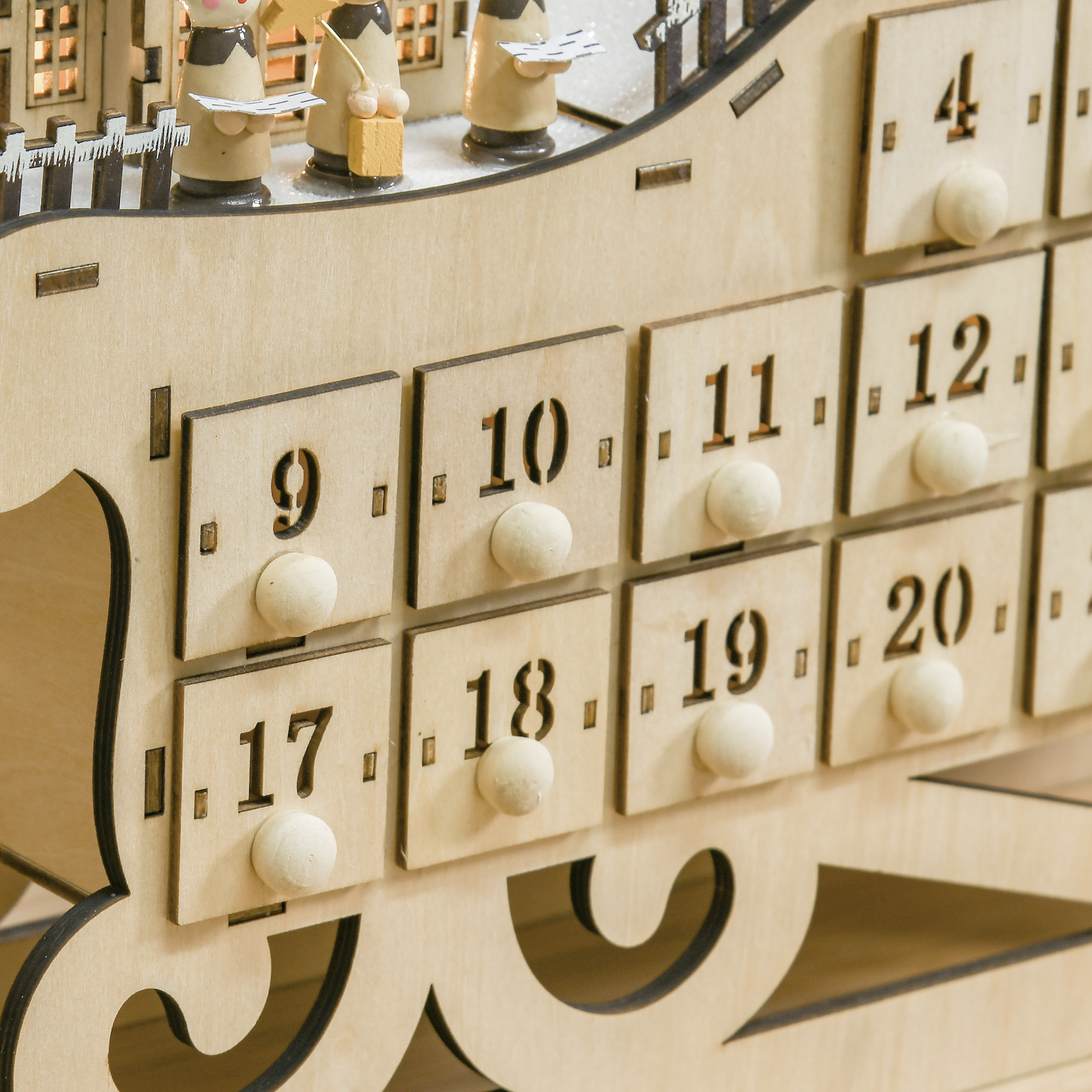 Calendario de adviento de madera con cajones numerados, figuritas en la parte superior, nieve y edificios.