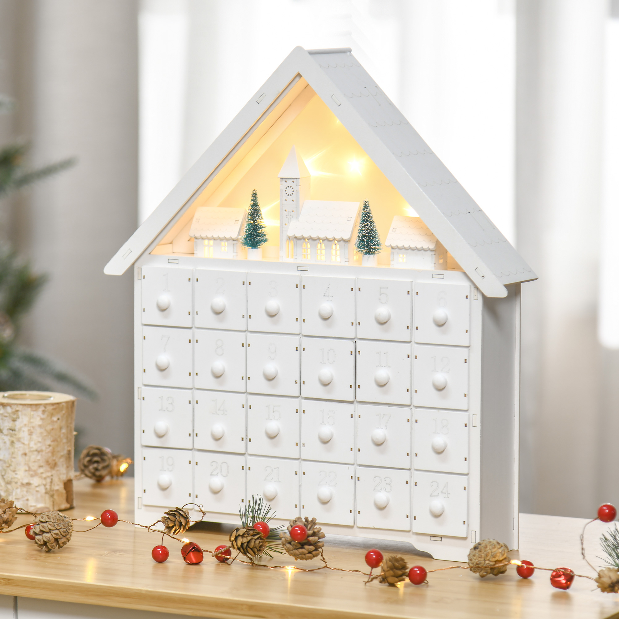 Calendario de adviento con forma de casa de madera blanca con cajones, números y luces decorativas. Fondo borroso.