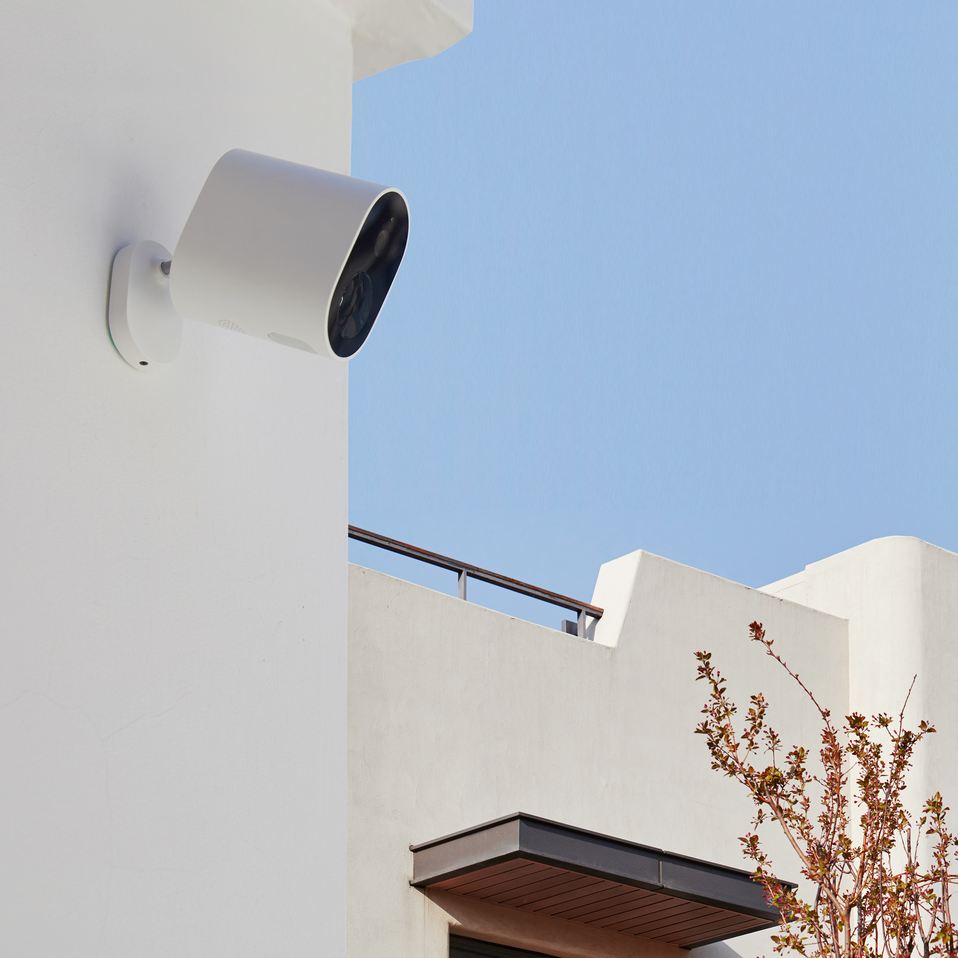 Telecamera di sicurezza bianca montata su un muro bianco, con cielo blu ed edificio sullo sfondo.
