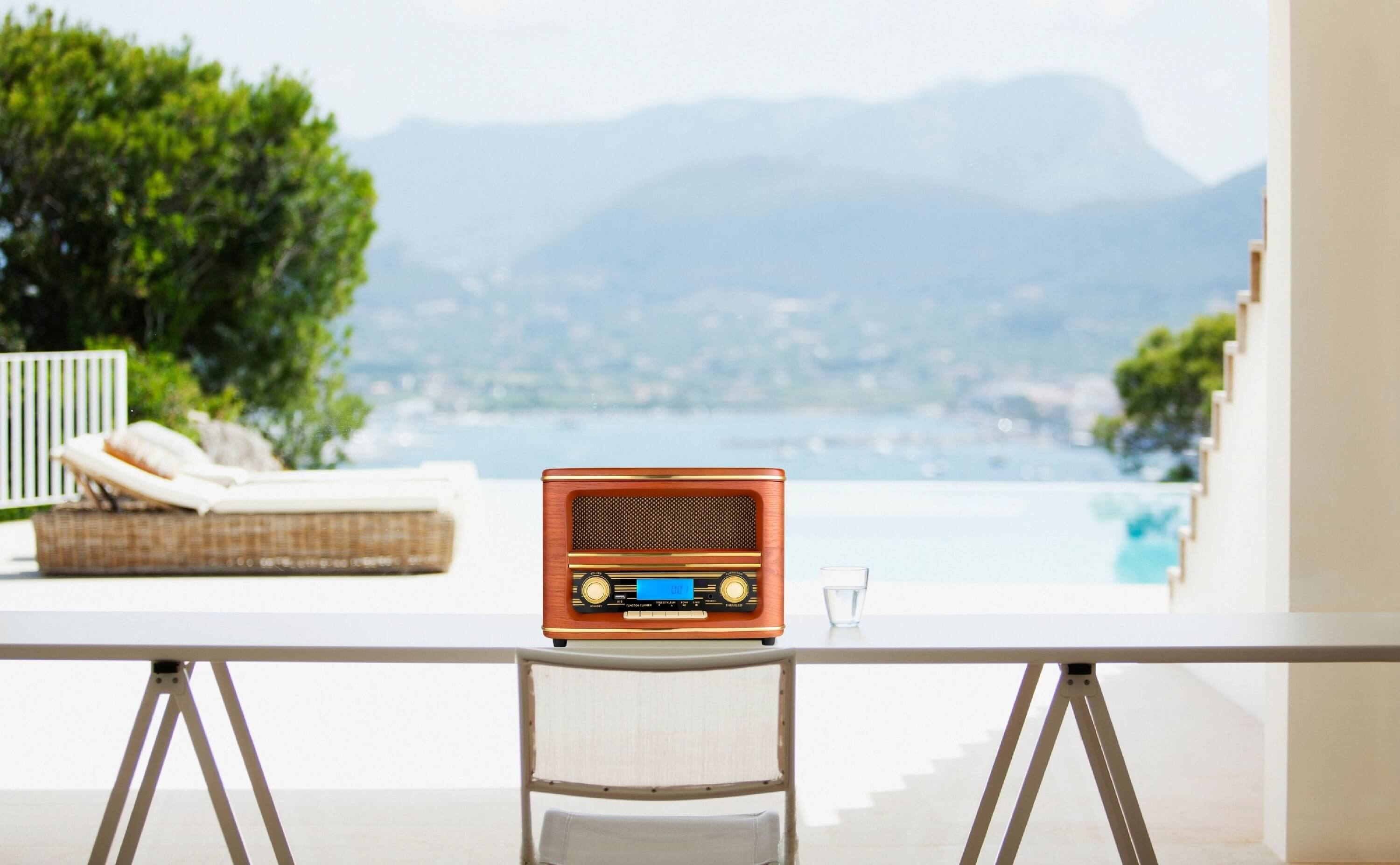 Vintage-Radio auf einem Tisch mit einem Glas Wasser. Berge und Meer im Hintergrund.