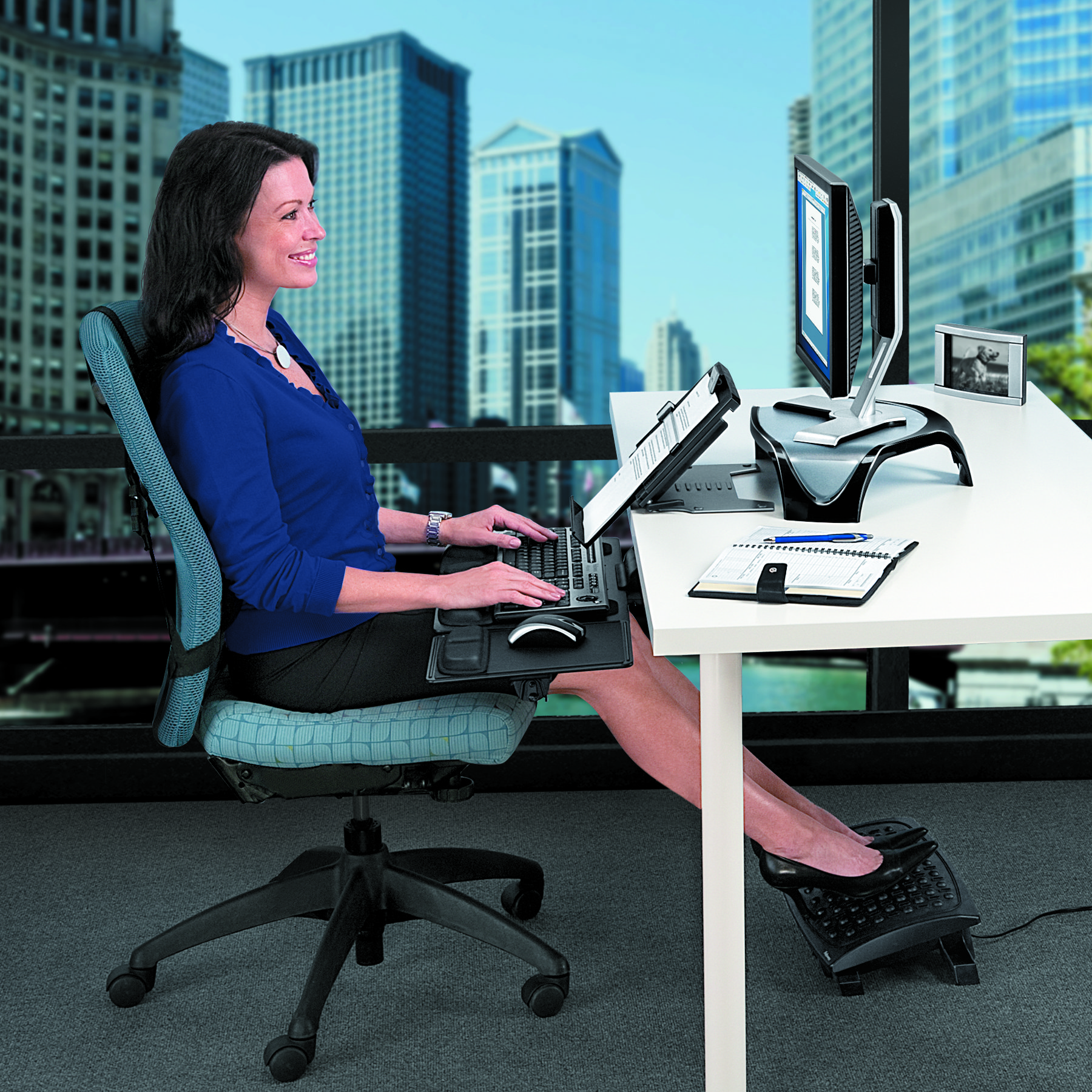 Donna alla scrivania che digita. C'è un computer e un poggiapiedi.