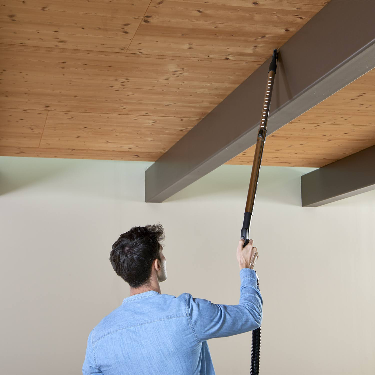 Un uomo che aspira una trave del soffitto. L'uomo è sullo sfondo, l'aspirapolvere in primo piano.