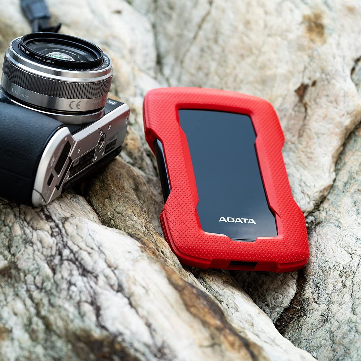 Aparat i czerwony dysk zewnętrzny ADATA na skale.