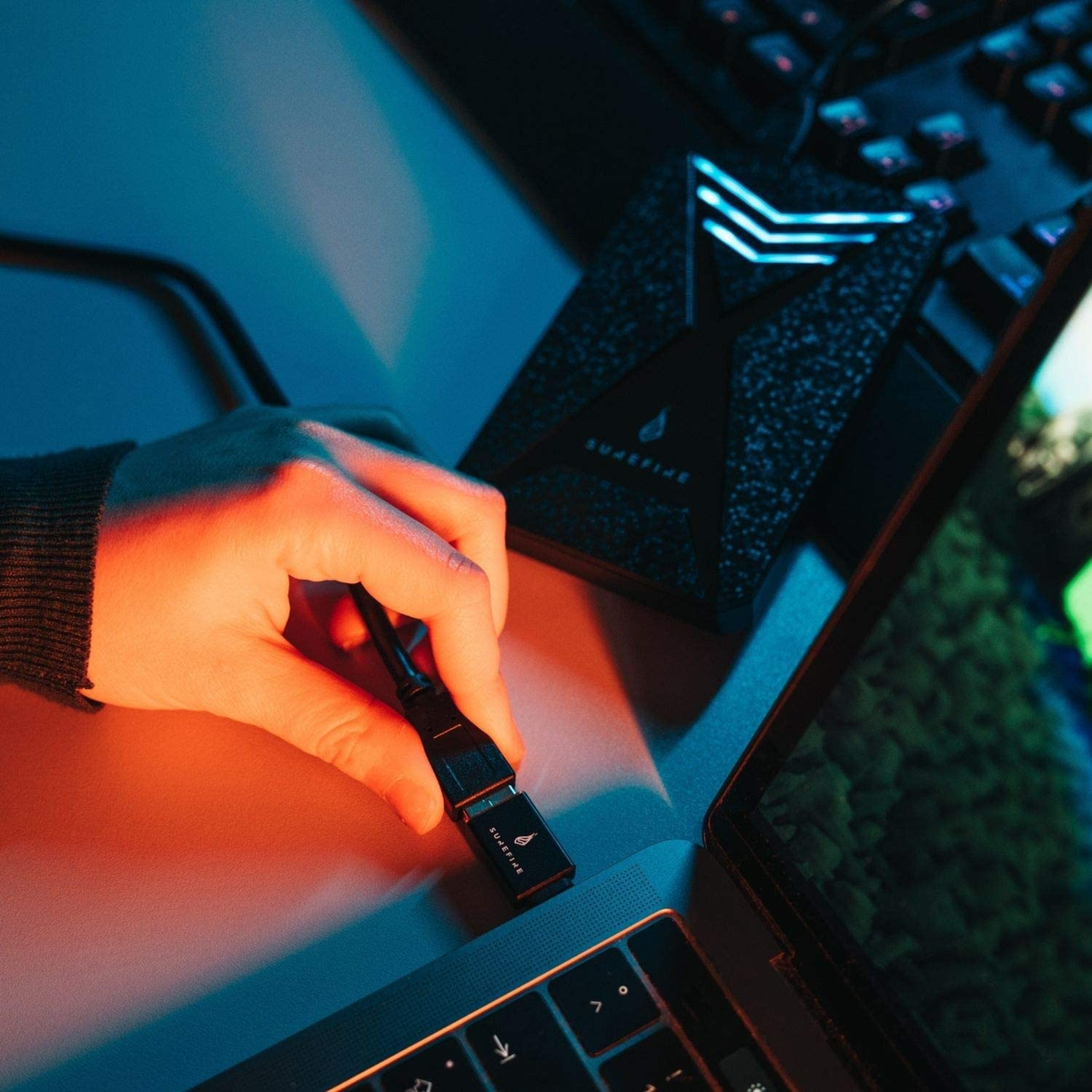 Dłoń podłączająca czarny kabel USB-C do czarnego urządzenia na laptopie, oświetlona niebieskim światłem.