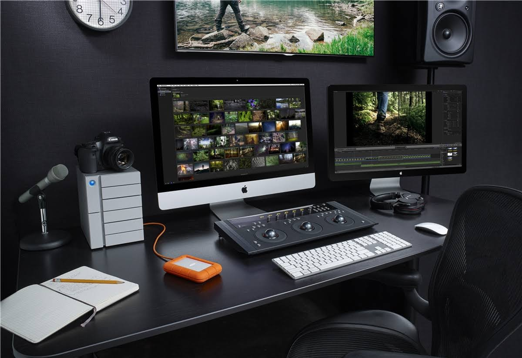 Konfiguracja biurka z dwoma monitorami komputera, aparatem i klawiaturą. Pokój jest ciemny i nowoczesny.