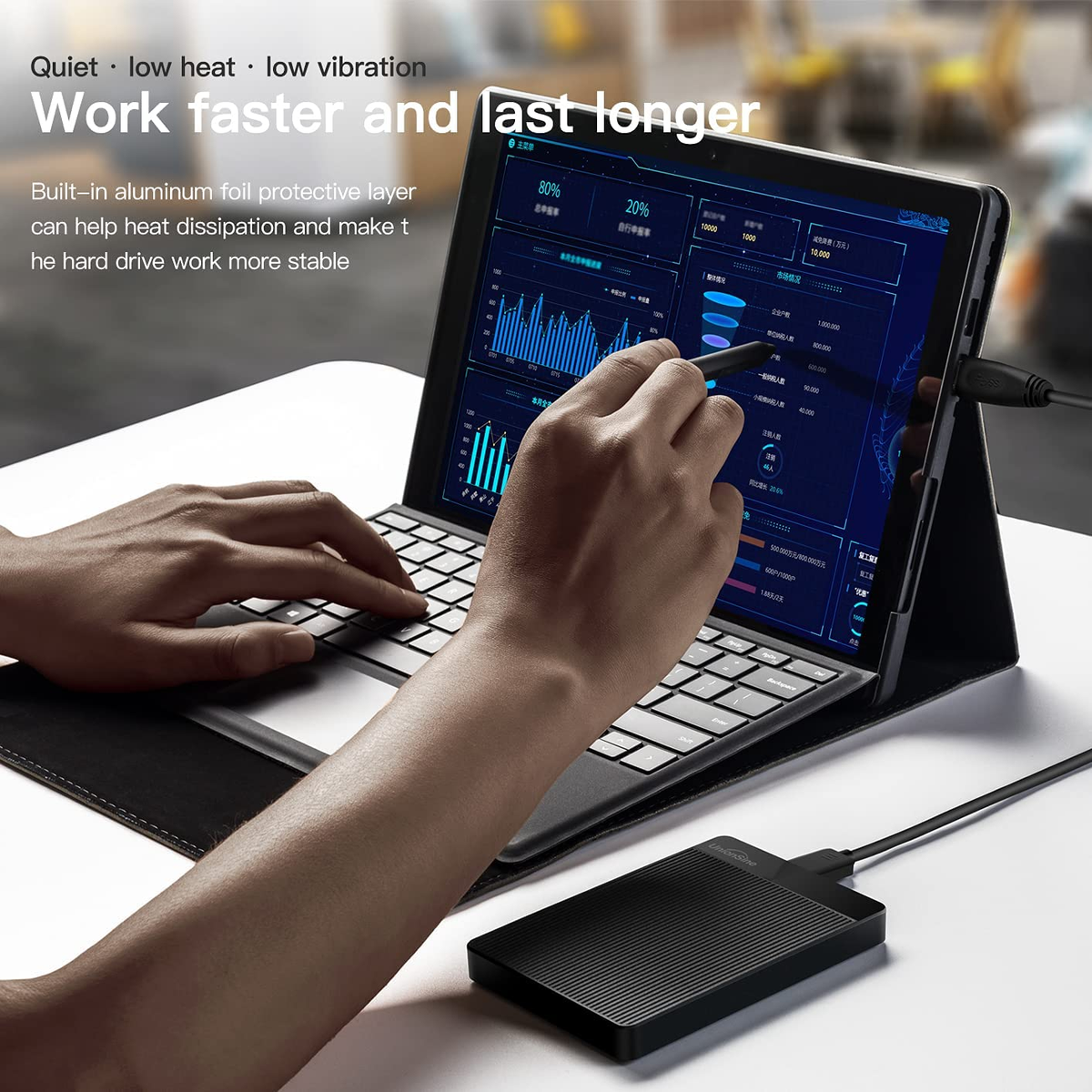 Una persona usando una tableta con teclado adjunto y un disco duro externo.