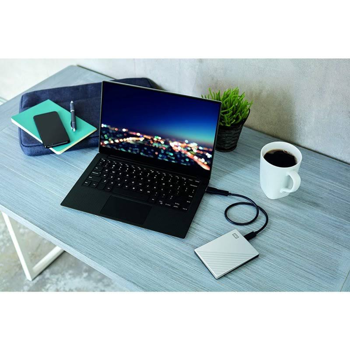 Laptop podłączony do białego dysku twardego, filiżanka kawy i smartfon na biurku.