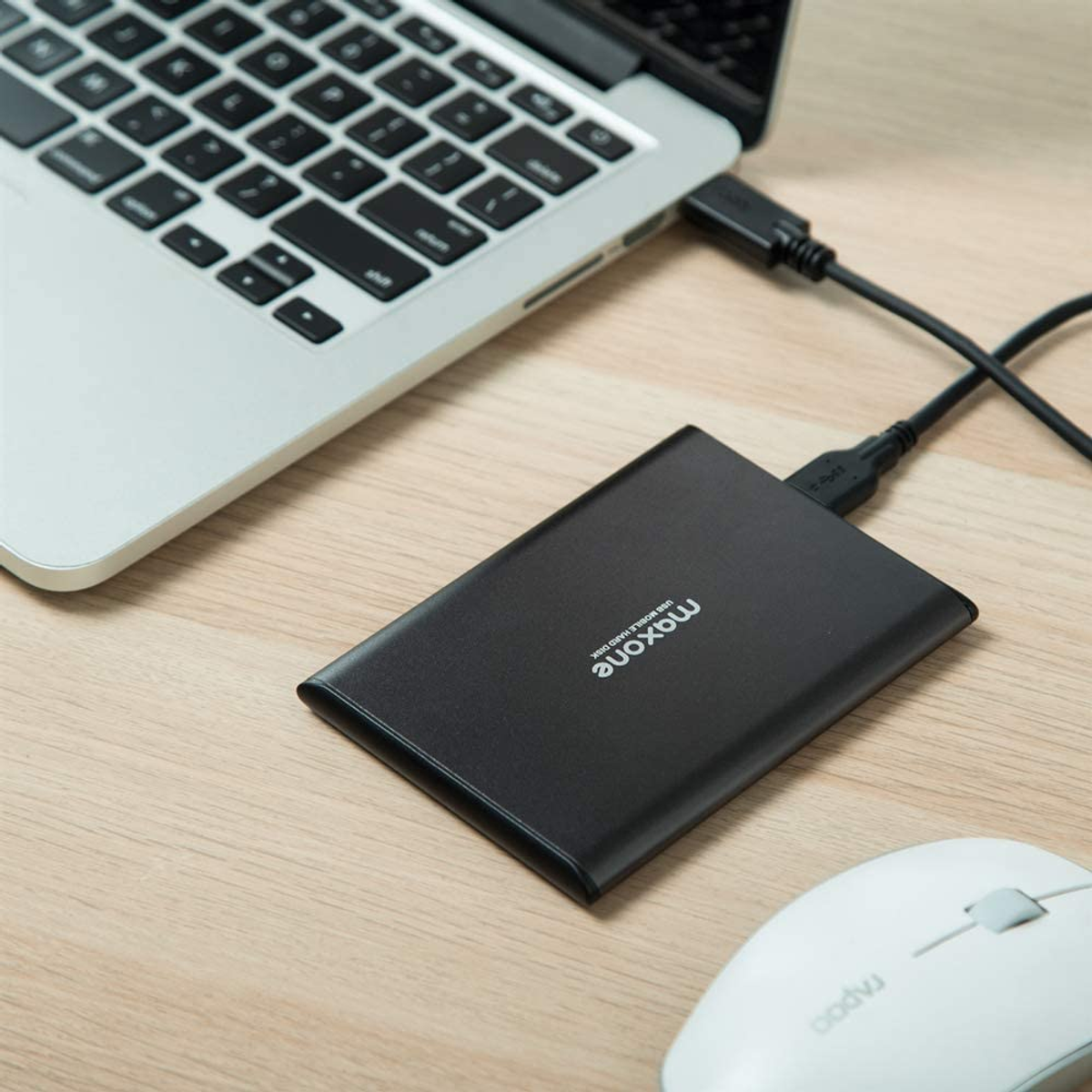 Disco rigido Maxone nero collegato a un laptop. Un mouse bianco è sulla superficie di legno.