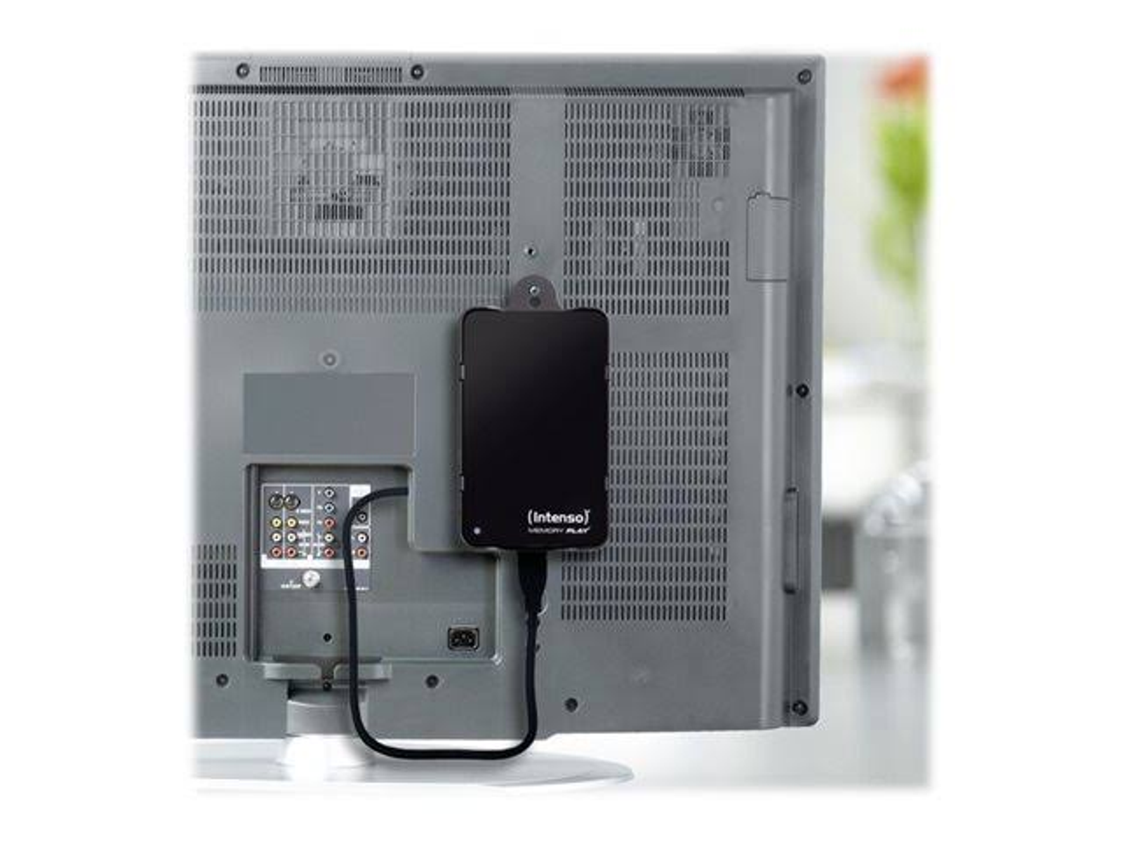 Czarny zewnętrzny dysk twardy podłączony do tyłu telewizora. Kable są podłączone. Szary telewizor.