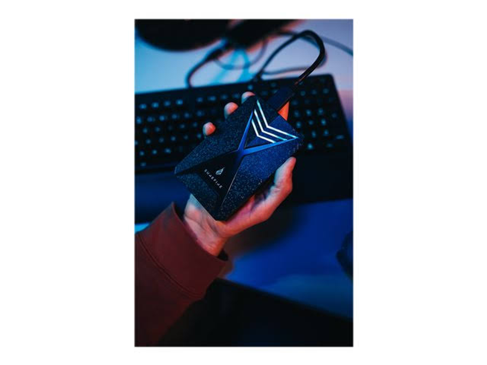 Dłoń trzymająca czarny zewnętrzny dysk twardy o unikalnym wzornictwie w pobliżu klawiatury.