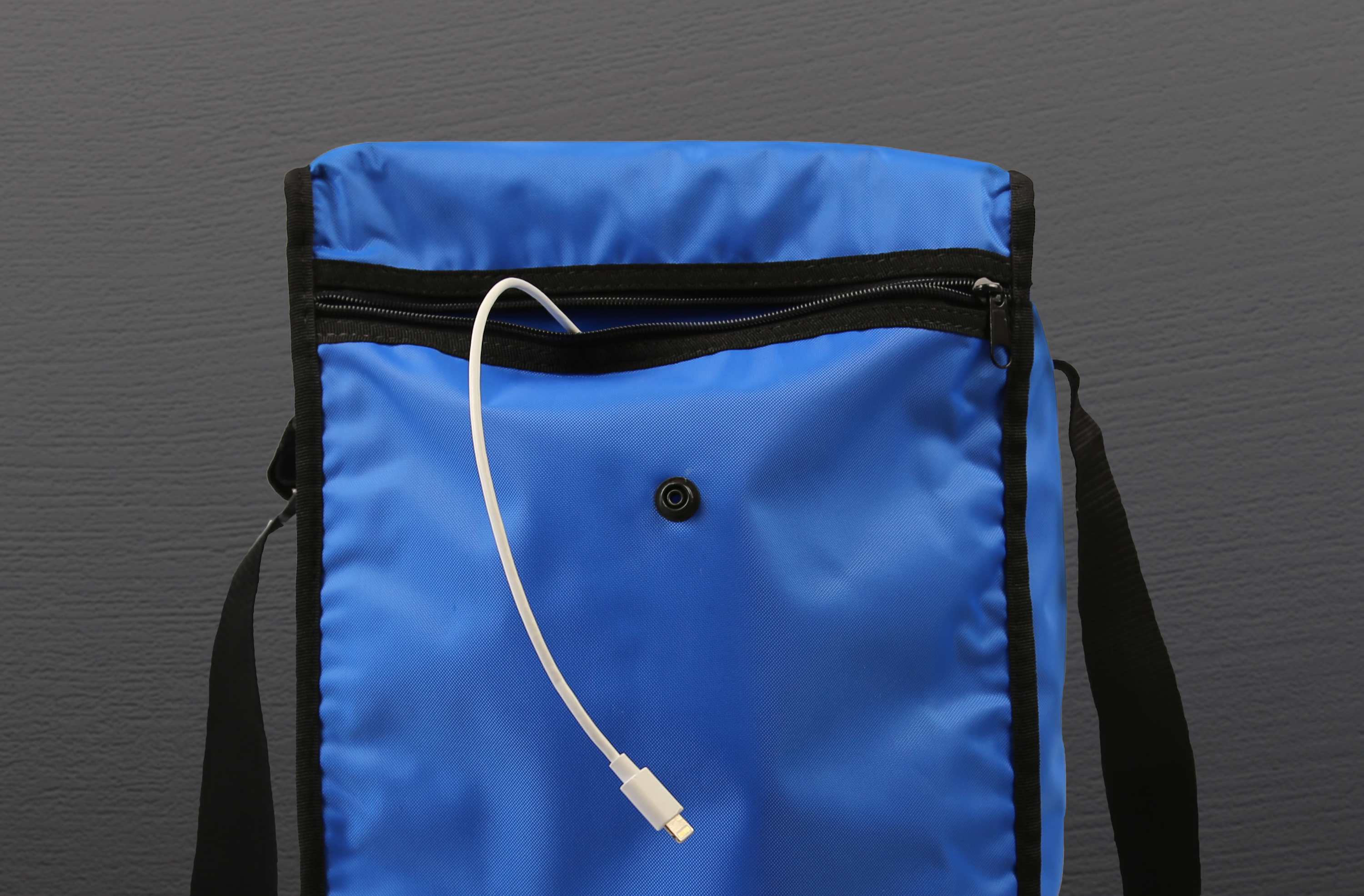 Eine blaue Tasche mit schwarzem Besatz. Ein weißes Ladekabel kommt aus einem Loch auf der Vorderseite.