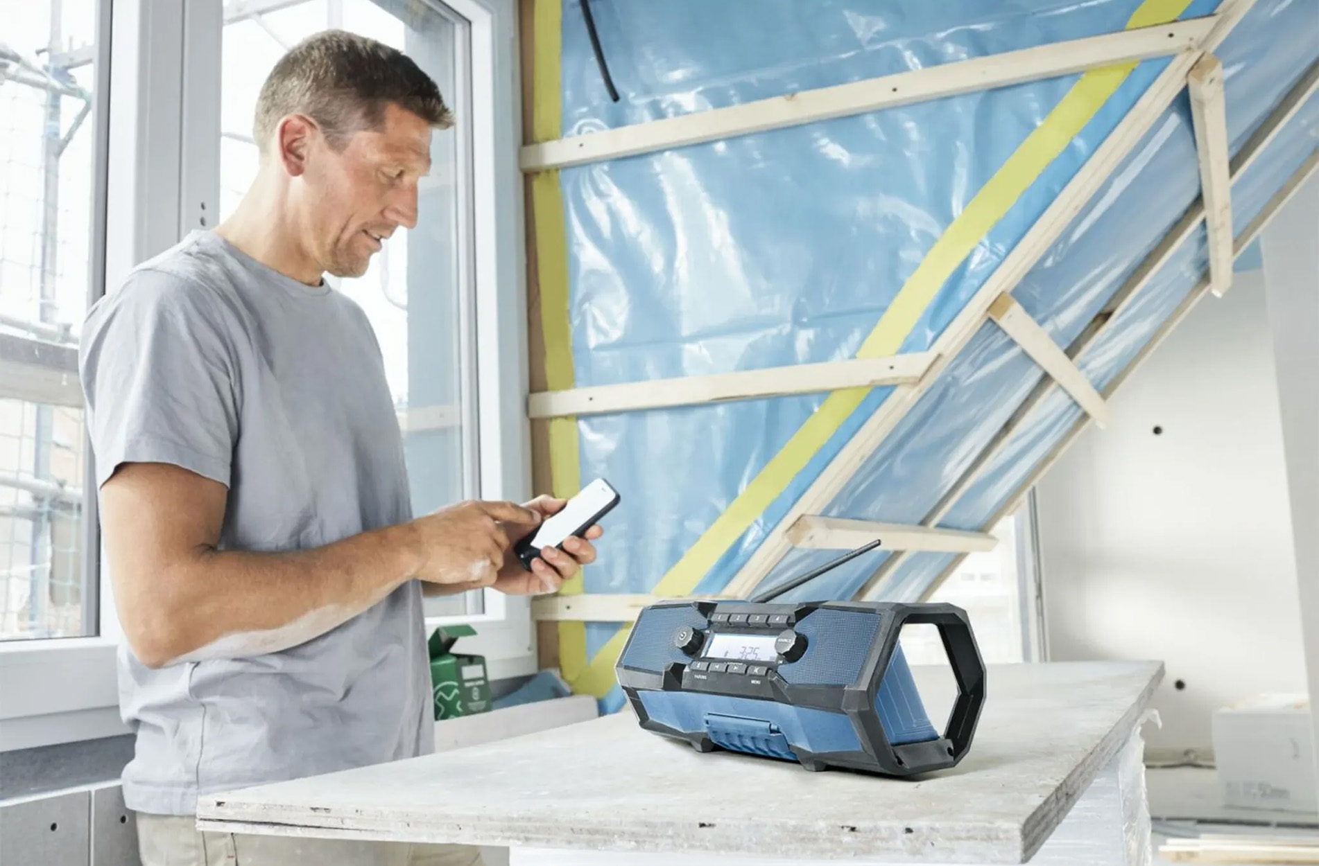 Mężczyzna używa smartfona obok niebiesko-czarnego radia na drewnianej powierzchni konstrukcyjnej.