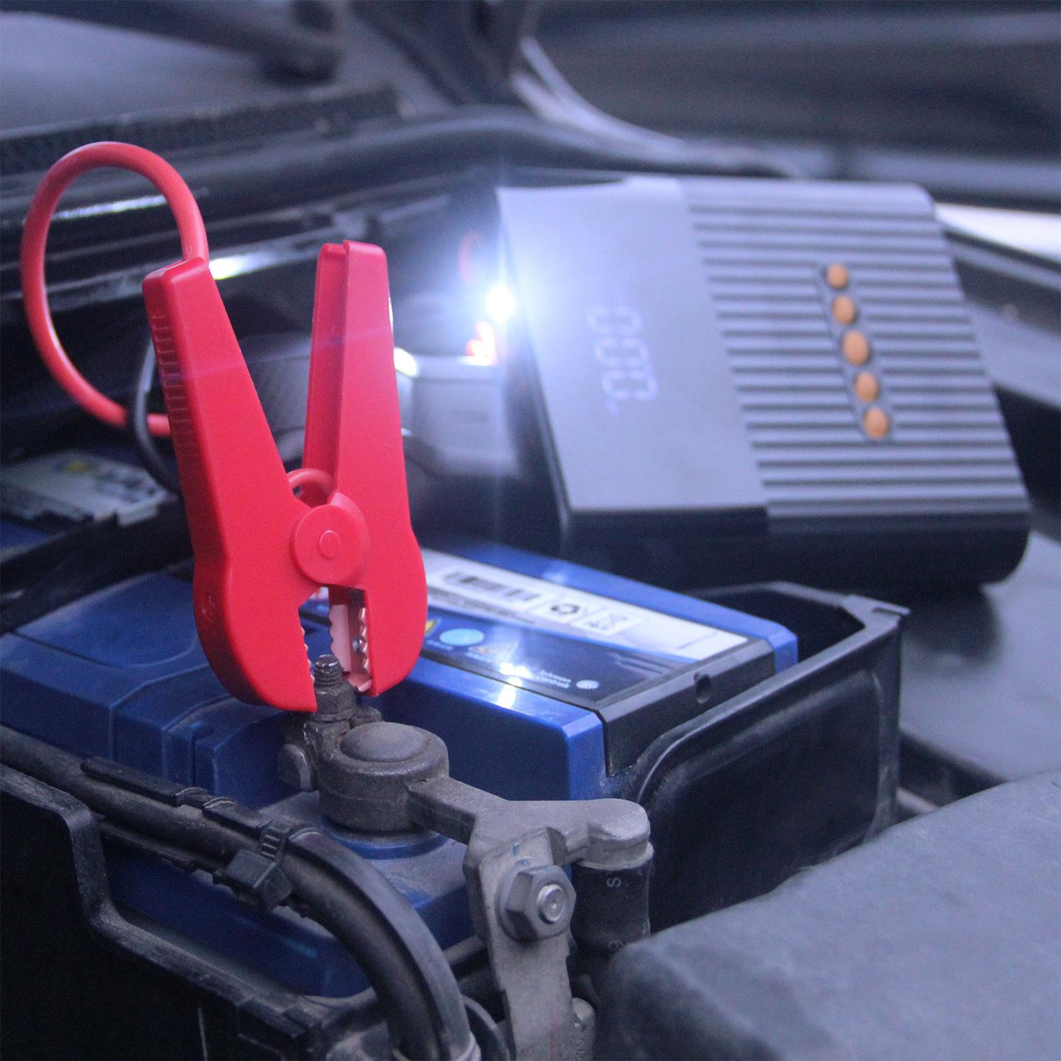 Una batteria per auto con cavi di avviamento collegati. Un caricabatterie sullo sfondo.